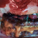 Close up of a double cheese burger with pickle, tomato spilling out